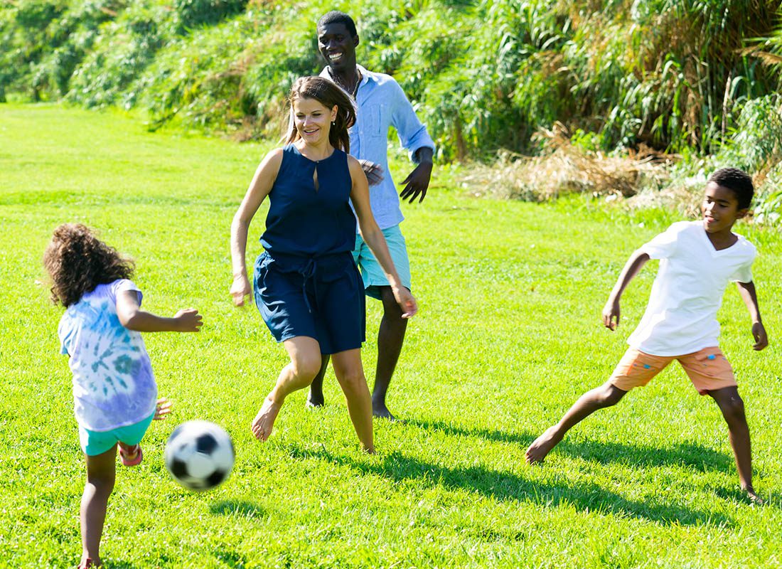 Employee Benefits - Happy Family and Their Two Children Playing Soccer on the Grass on a Sunny Day